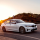 A photo of a white BMW 330e sedan driving at sunset.